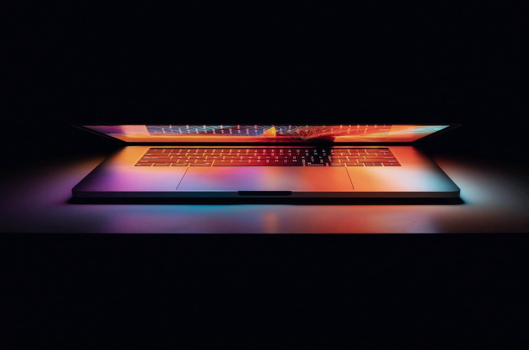 A laptop in a dark room, its screen glowing with colour